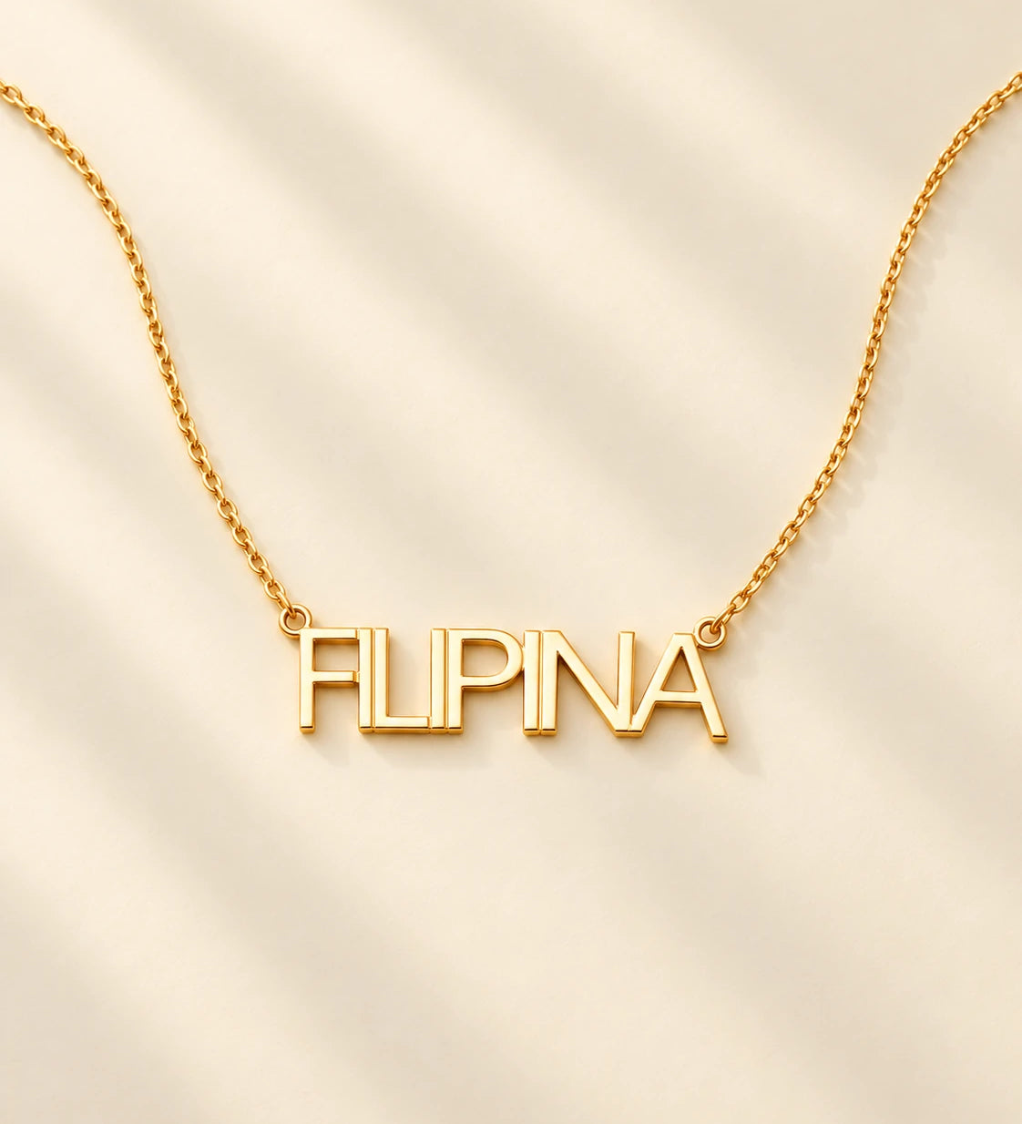 FLEURENZ FILIPINA uppercase 14k gold-filled nameplate necklace on an ivory background