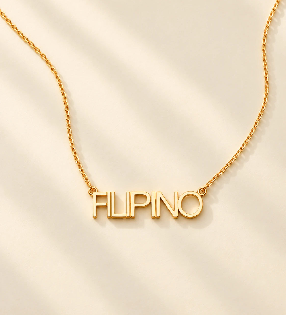 FLEURENZ FILIPINO uppercase 14k gold-filled nameplate necklace on an ivory background